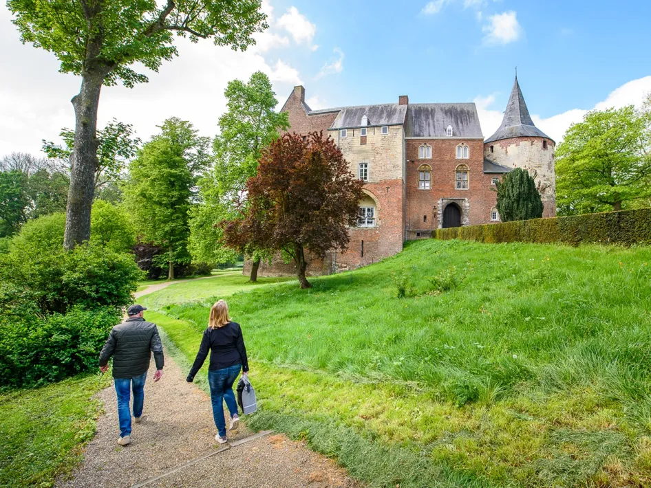 Wandelaars lopen over een grindpad langs het groene terrein van Kasteel Horn, met het kasteel en de ronde toren op de achtergrond tijdens de kunstwandeling - wanjele door Häör.