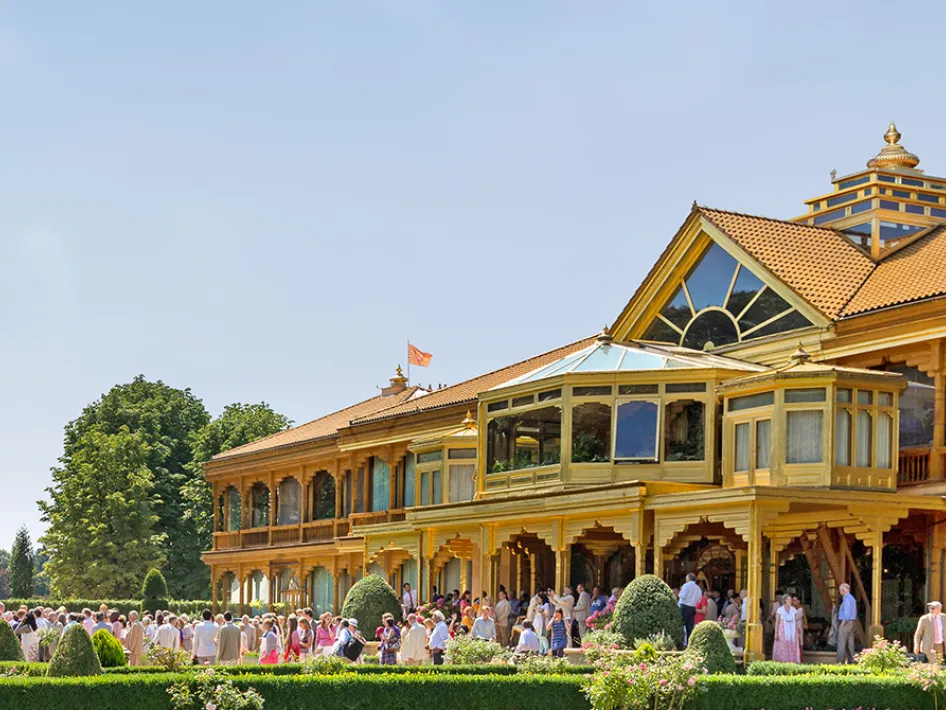 Bezoekers verzamelen zich bij het houten hoofdgebouw van MERU in Vlodrop tijdens Wereld Meditatie Dag, op een zonnige dag tussen groen en sierlijke architectuur.