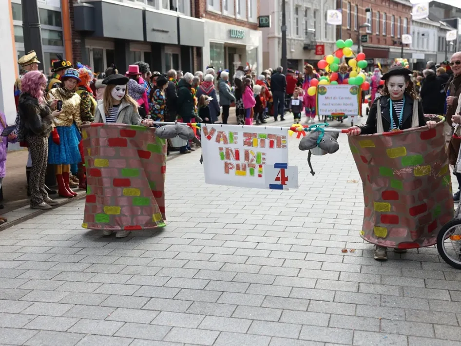 Kinderen in kleurrijke kostuums lopen mee in de Wichteroptocht in Weert, terwijl toeschouwers langs de kant toekijken.