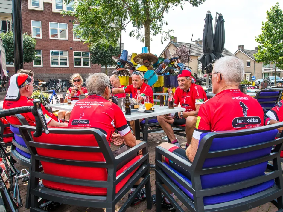 A group of road cyclists takes a break on a terrace, with their bikes nearby.