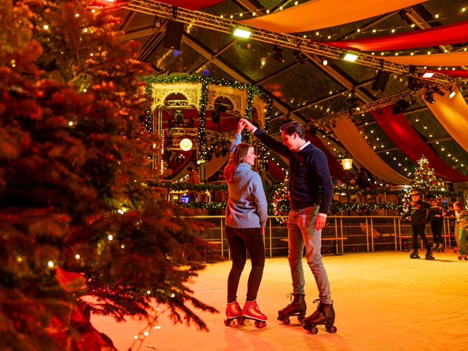 Ein Mann und eine Frau fahren gemeinsam Rollschuh in der festlich geschmückten und stimmungsvoll beleuchteten Winter Fever Arena.