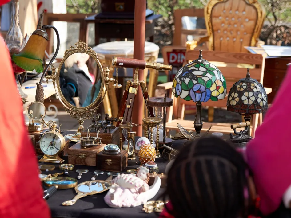 Kraam met vintage spullen, lampen en spiegels tijdens de rommelmarkt op de Zomerfeesten Beegden, met bezoekers op de voorgrond.