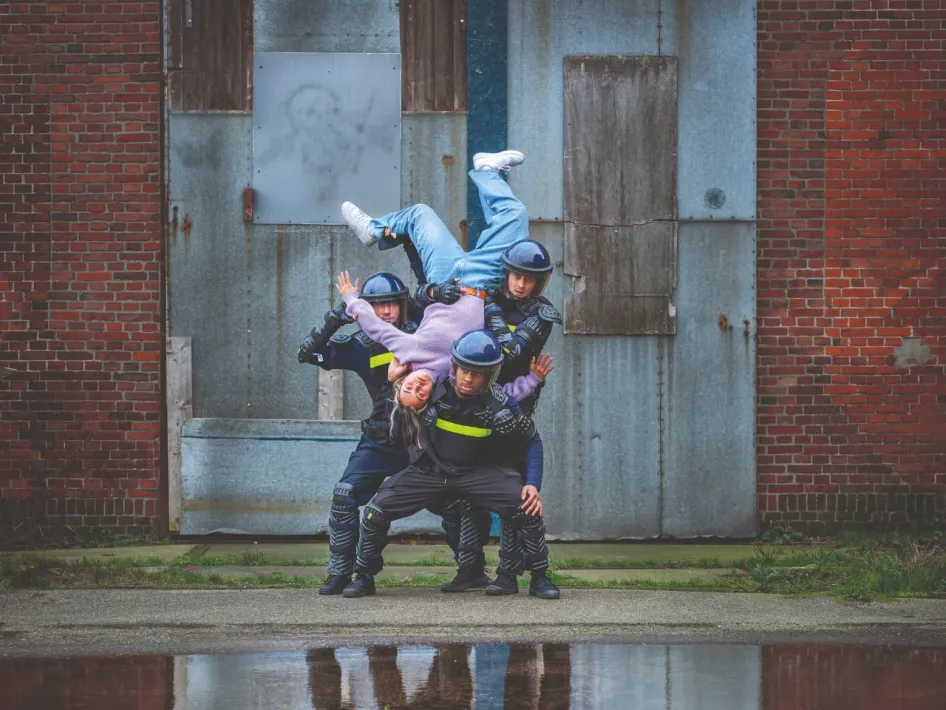 Drie dansers in ME-uniformen tillen een vierde danser ondersteboven tijdens een scène uit de theatervoorstelling CONTRA.