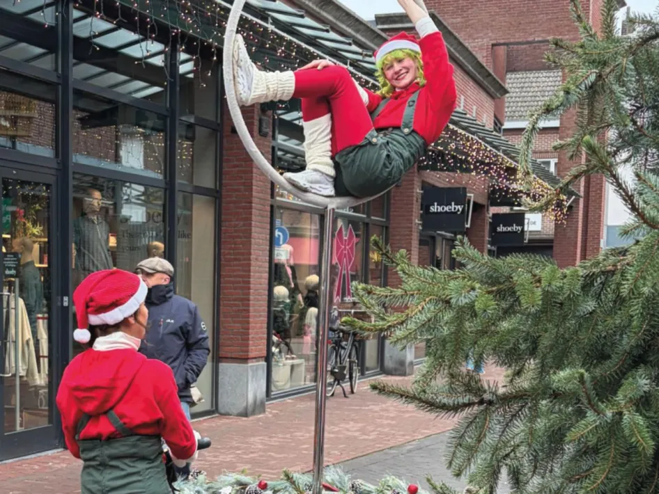 Een artiest in kerstkleding voert een acrobatische act uit in een ring boven een winkelstraat in Echt, tijdens Winters Vermaak.