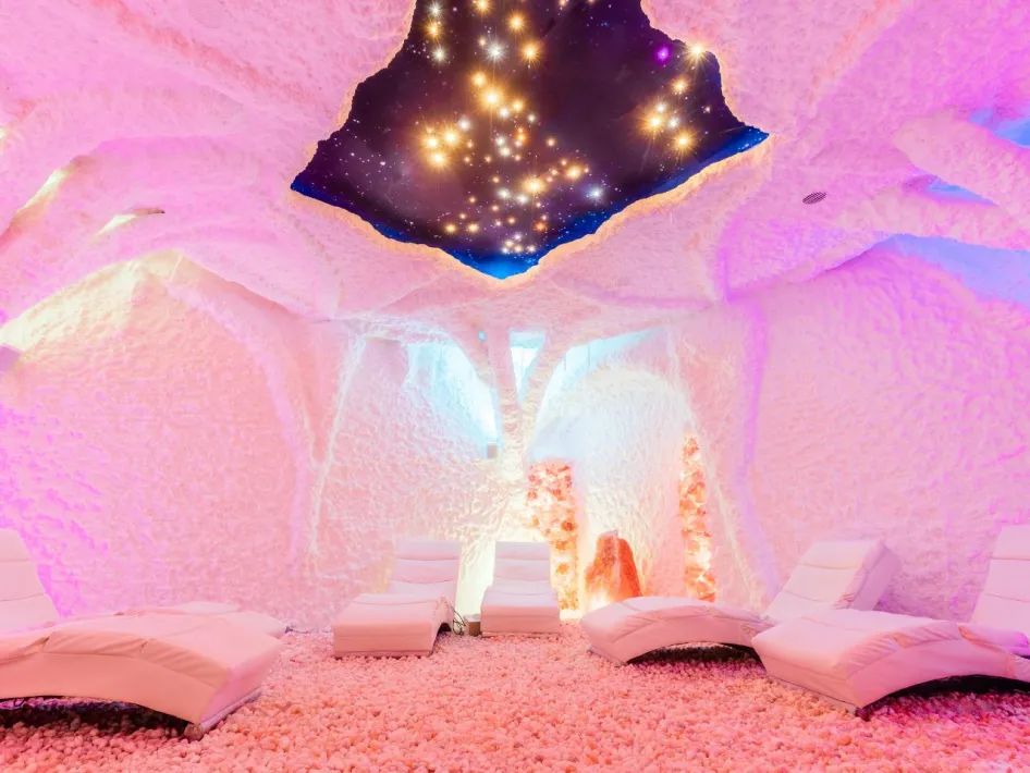 Wellnessruimte met ligstoelen in een kleurrijk verlichte zoutkamer met sterrenhemel bij Zout & Zo.