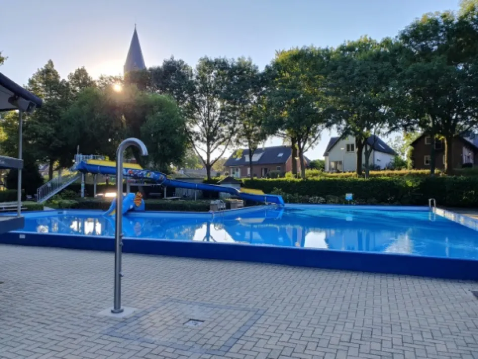 Zwembad Weerderhof in Linne met glijbaan, ligweide en bomen rondom het water.