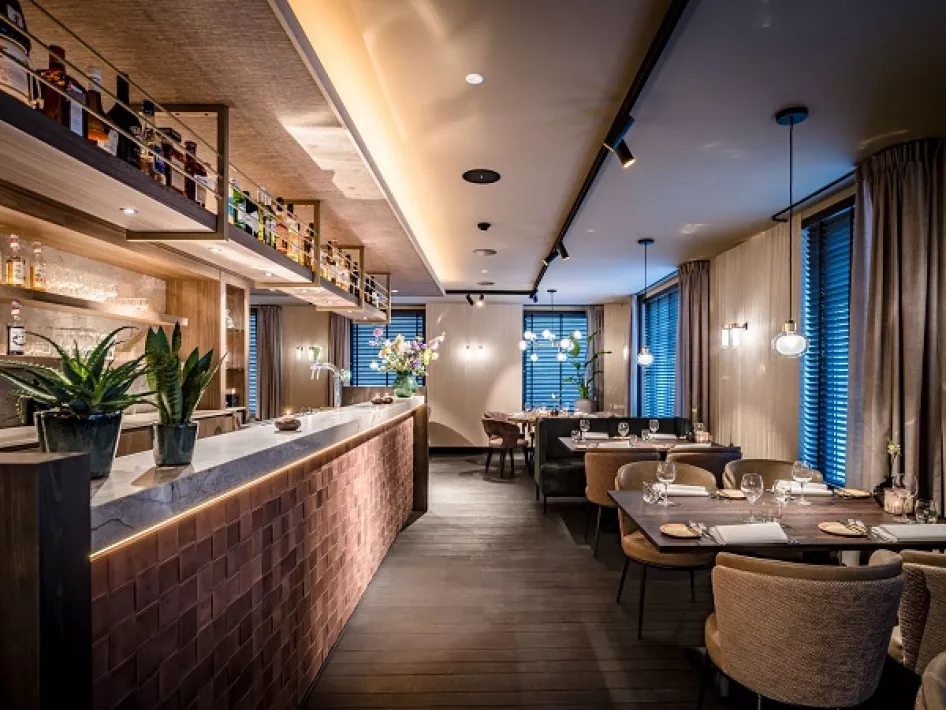 Modern restaurantinterieur met sfeervolle verlichting, een stijlvolle bar en luxe gedekte tafels.