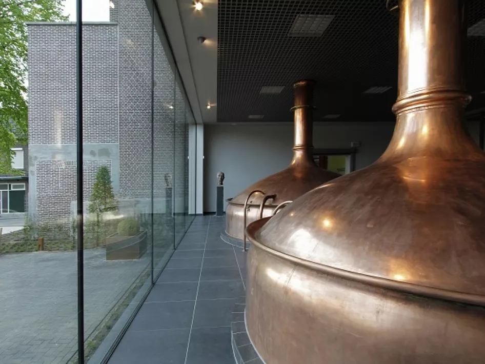 Twee glanzende koperen ketels in een strak en modern interieur met uitzicht op buiten via grote ramen.