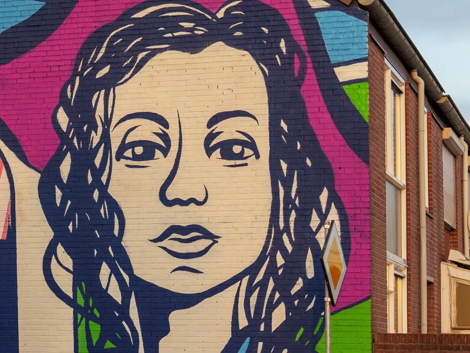 Muurschildering van een vrouwenportret in felle kleuren op de zijgevel van een woonhuis.