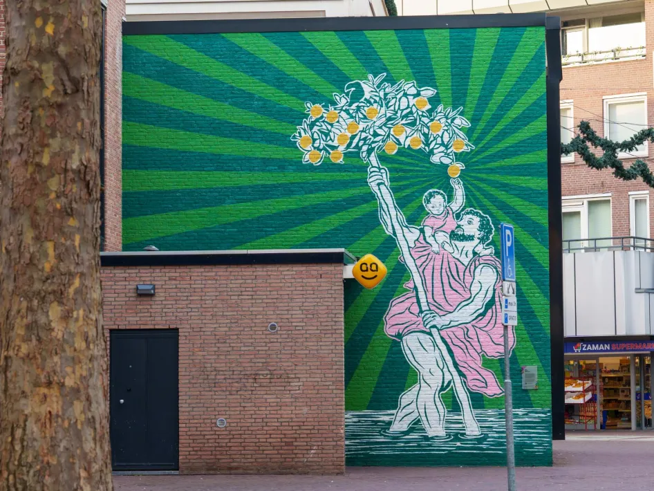 Muurschildering van Sint-Christoffel (Sjtuf) met een kind op zijn arm die samen een tak met sinaasappels omhooghouden.