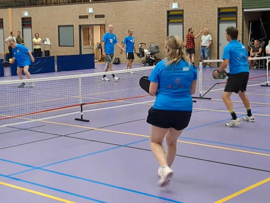 Pickleballspelers in blauwe shirts spelen een dubbelwedstrijd tijdens de Limburg Open Pickleball.