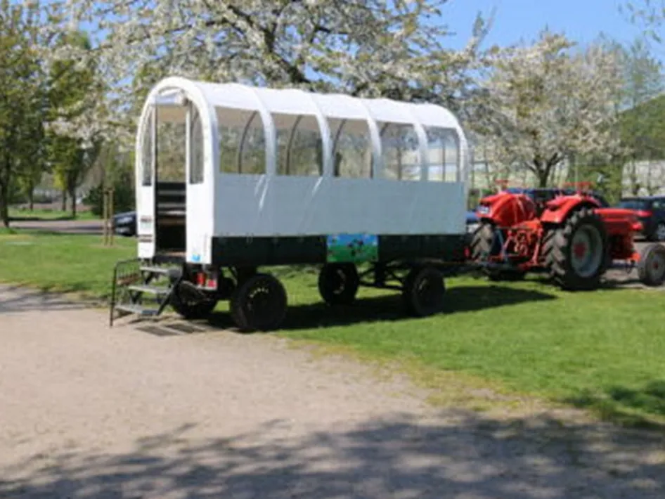 Huifkar achter een rode tractor op het terrein van het museum, waar bezoekers na het timmeren een huifkarrit kunnen maken.