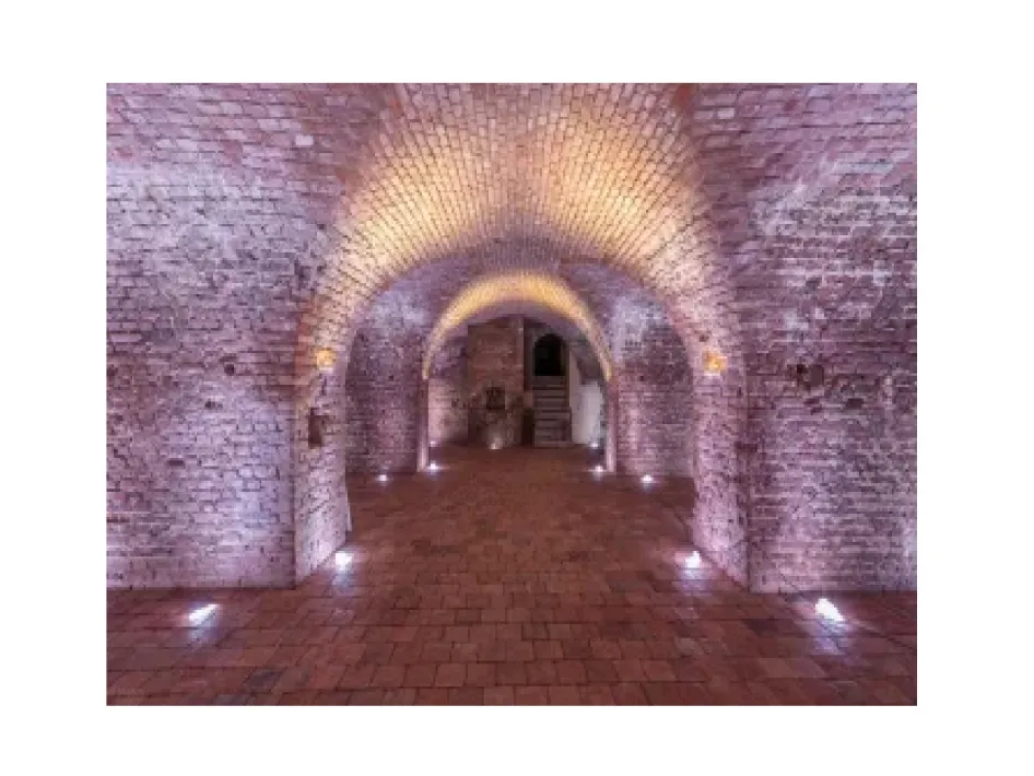 Gewelfde bakstenen ruimte in Kasteel Montfort met sfeervolle verlichting langs de muren.