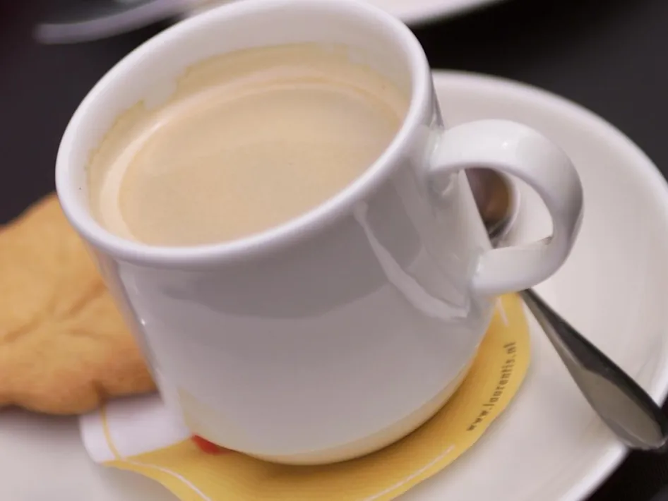 Kaffee in einer weißen Tasse, ein Keks und ein Löffelchen auf einer weißen Untertasse vom High Tea