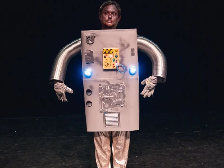 Diederik Jekel verkleed als robot met doosvormig kostuum en metalen armen tijdens een theatervoorstelling