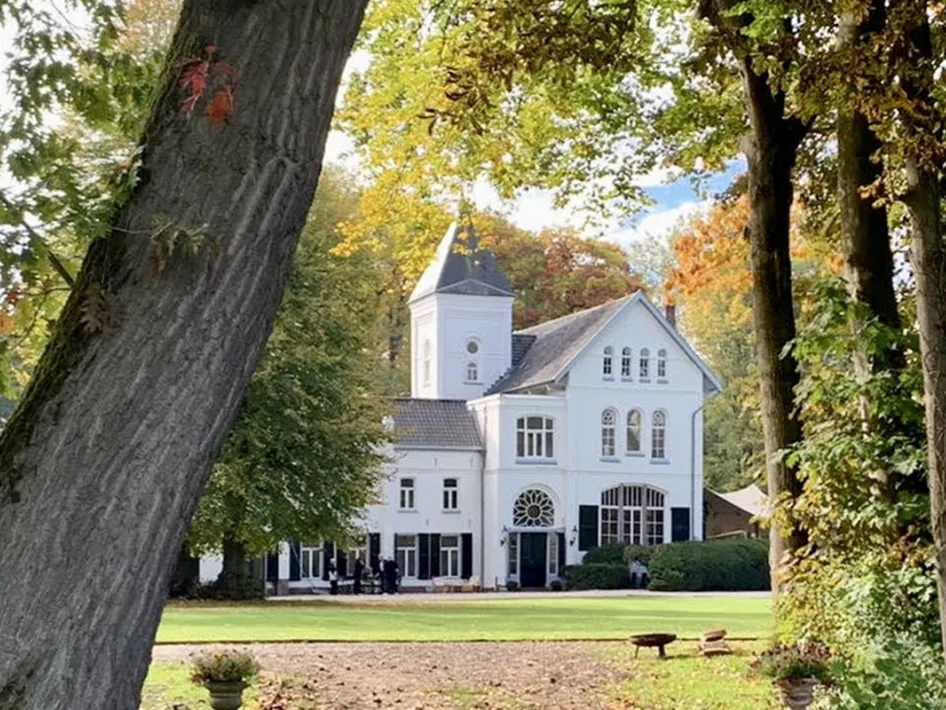 Voormalig kloostergebouw in een parkachtige omgeving, met hoge bomen en herfstbladeren in de tuin op Landgoed Frymerson.