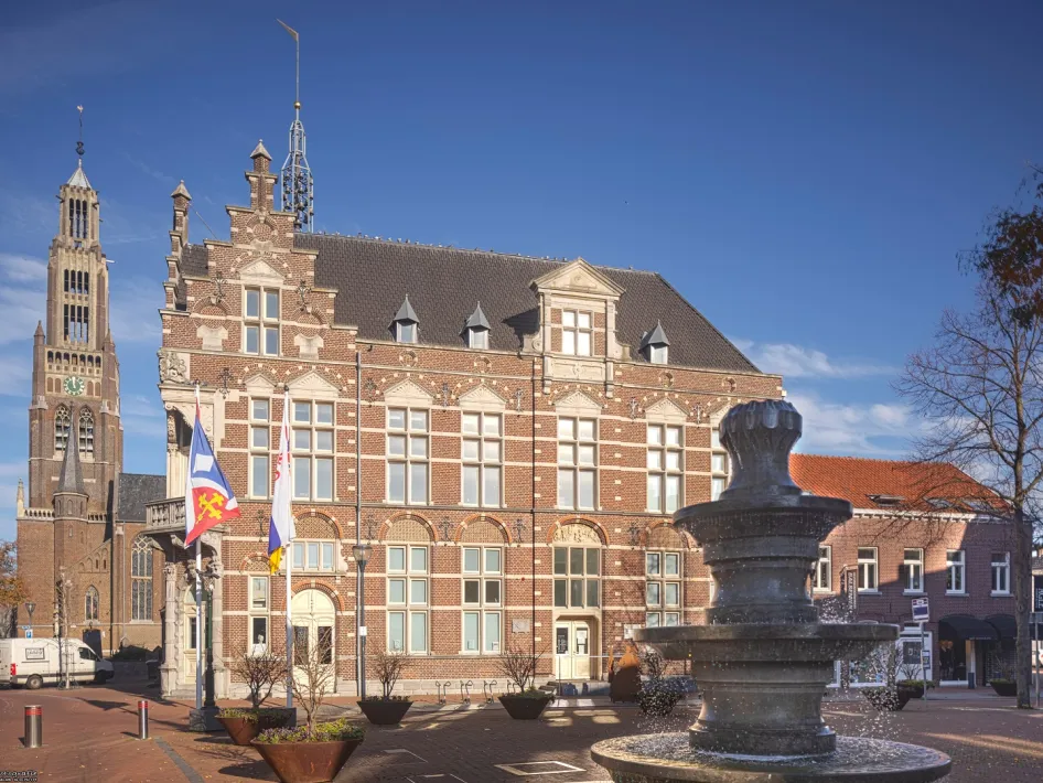 Het historische gebouw van Museum van de Vrouw in Echt, met fontein op het plein en de kerk op de achtergrond, gefotografeerd bij helder weer