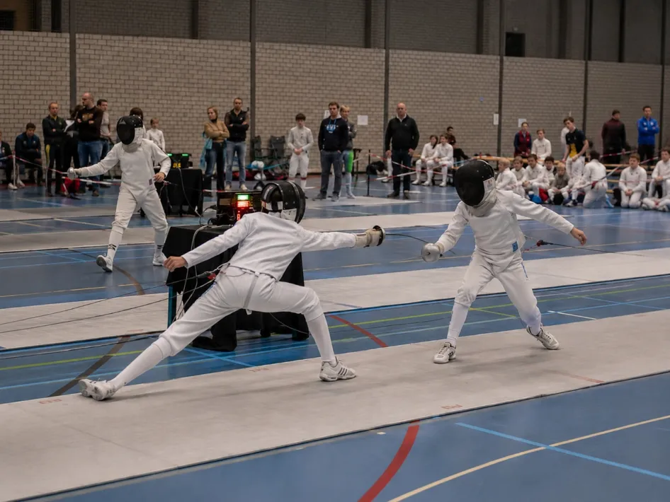 Jonge schermers in actie tijdens een wedstrijd schermen in een sporthal.