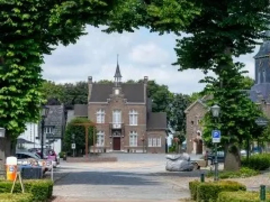 Dorpsplein in Stevensweert met zicht op het Maaseiland Museum, omringd door groen en omlijst door bomen.