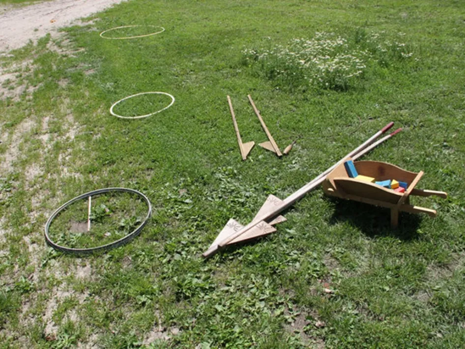 Materialen voor oud-hollandse spelen op het gras, met houten spelstukken, ringen en een kruiwagen voor traditionele buitenspellen.