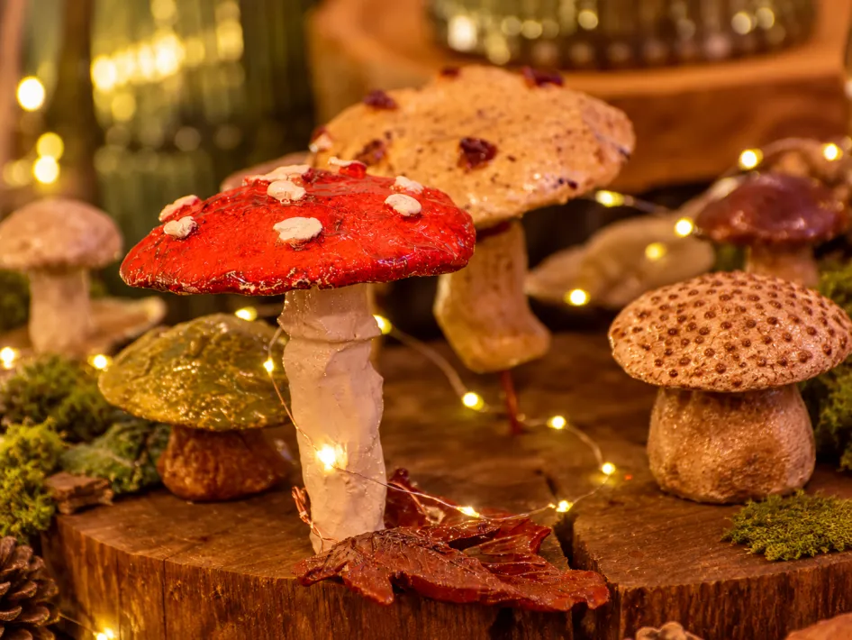 Decoratieve paddenstoelen met lichtjes op een houten ondergrond, met een rode paddenstoel op de voorgrond.