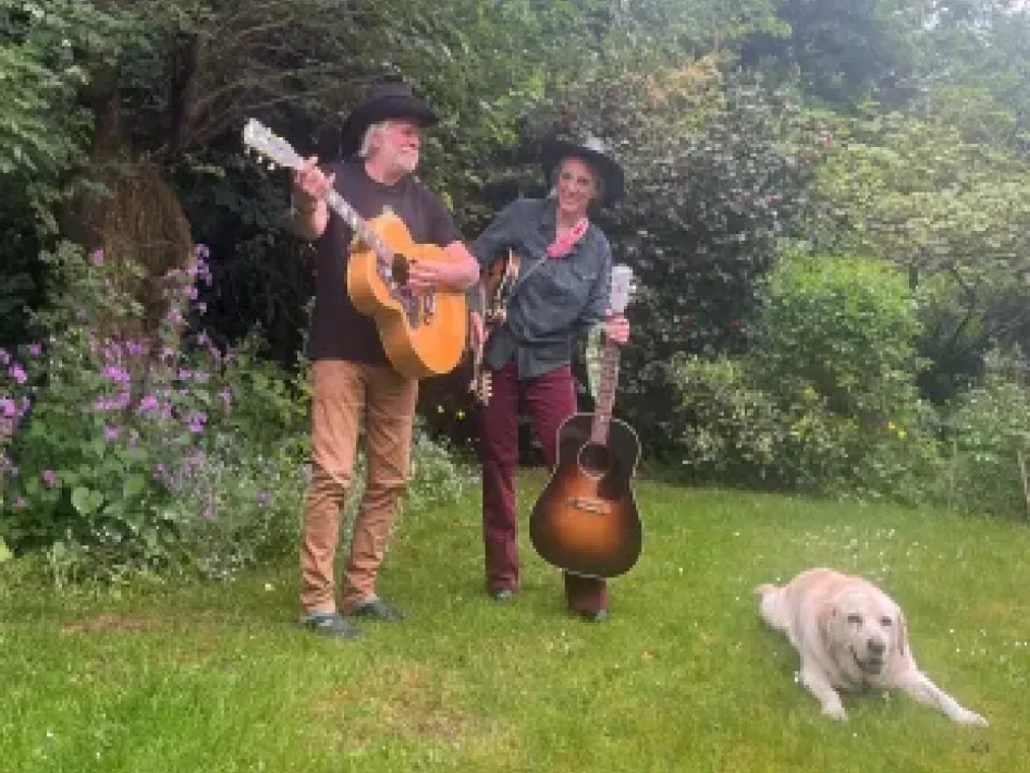 Muzikaal duo met gitaren staat in een groene tuin voor een optreden op het Peelpodium.