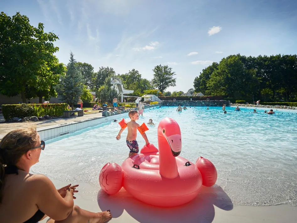 Kinderen spetteren in het buitenzwembad tijdens het zwemmen bij de Leistert, omringd door ligstoelen en zomerzon.