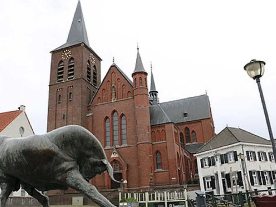 Standbeeld van een stier tijdens een rondleiding in Wessem, met op de achtergrond de rode Sint Medarduskerk en omliggende bebouwing.