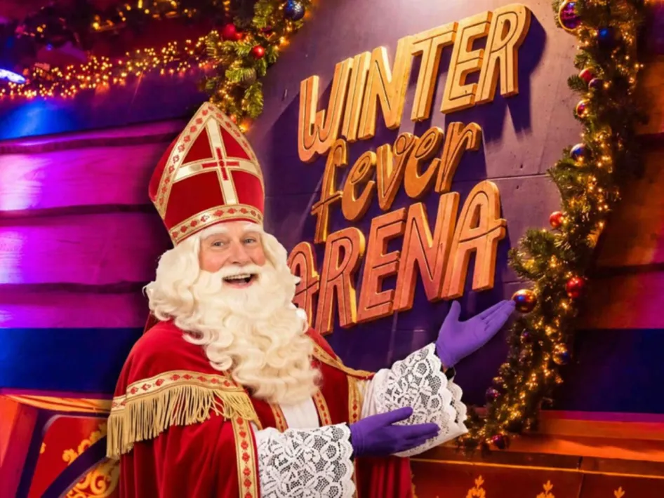 Sinterklaas in zijn rode mantel en mijter bij het verlichte bord van de Winter Fever Arena, omringd door kerstversiering.