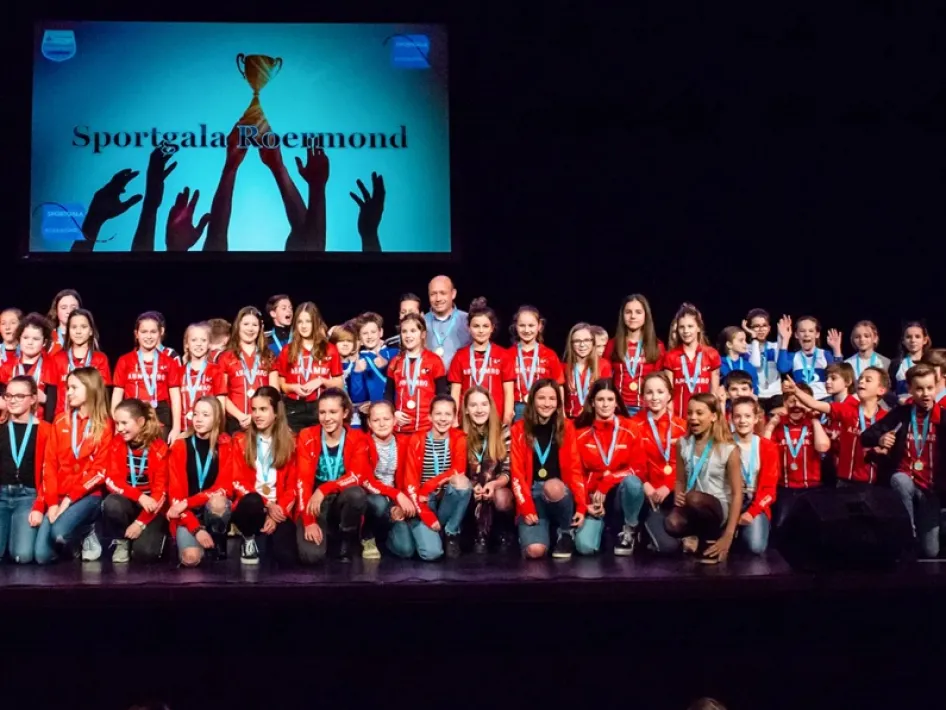 Sportgala Roermond met een grote groep kinderen en jongeren op het podium die medailles dragen en samen hun sportprestaties vieren.