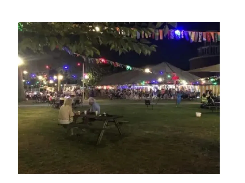 foto van mensen die zitten op een bankje voor een tent tijdens zomerfeest fatimapark in weert