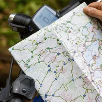 Fietser bekijkt de nieuwe fietsknooppuntenkaart Noord- en Midden-Limburg 2025 op het stuur, omringd door groen.