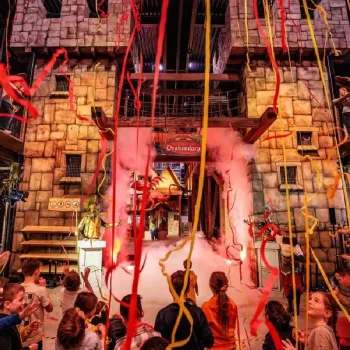 Kinderen en ouders vieren de opening van Drakendorp met slingers en rook bij een grote kasteelpoort.