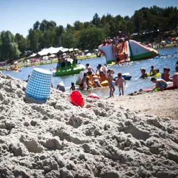 Drukbezochte zwemlocatie in Hart van Limburg met spelende kinderen, zandstrand en opblaasbaar waterpark.