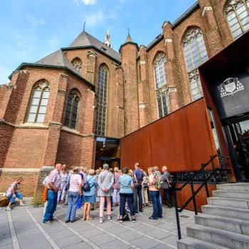 Groep mensen bij de ingang van het Historiehuis in Roermond, met op de achtergrond de oude gevel van de Munsterkerk.