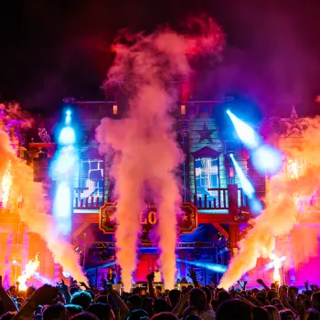 Bezoekers genieten van het Outrageous Festival in Leveroy met een verlicht hoofdpodium, vuur- en rookeffecten en een energieke festivalsfeer.