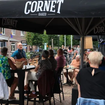 Publiek luistert naar live akoestische muziek tijdens het Akoestisch Festival Beesel op een sfeervol terras in het dorpscentrum.