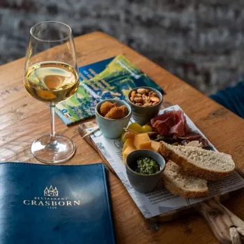 Borrelplank met brood, kaas, ham en witte wijn op tafel, naast het menu van Crasborn