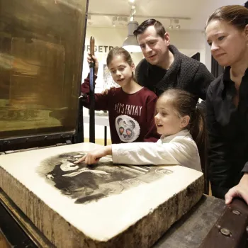 Gezin ontdekt de werking van een historische steendrukpers tijdens Drukkersdag in Eynderhoof.