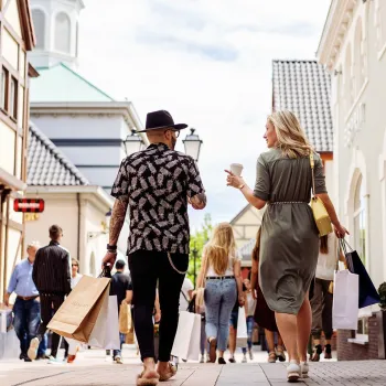 Two people walk together through a shopping street with shopping bags and coffee during the Friends & Family Event at Designer Outlet Roermond.