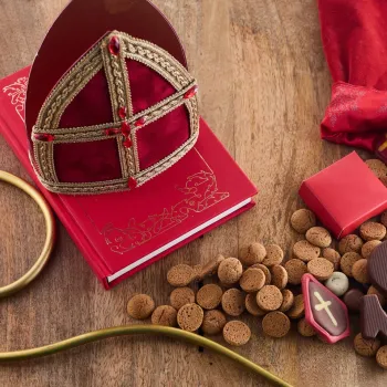 Op een houten tafel liggen een rode mijter, een staf, een rood boek, kruidnoten, chocoladeletters en cadeautjes naast een opengebroken jutezak in het Huis van Nicolaas in Weert.