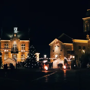 Een plein in Stevensweert met een grote kerstboom, verlichte gevels, vuurkorven en bezoekers die samen het Kaarsenfeest Stevensweert vieren.