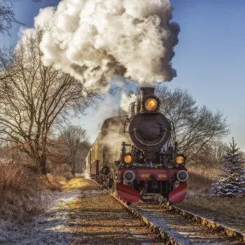 De stoomlocomotief van de Kerst Expres met rode details rijdt over een enkel spoor door een winters landschap langs de Miljoenenlijn.