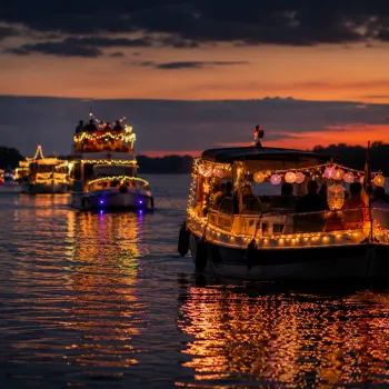 Lampionnentocht Roermond met sfeervol verlichte boten die in de avond over de Maas varen en weerspiegelen in het water.