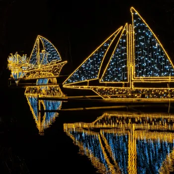 Verlichte bootvormige lampionnen weerspiegelen in het water tijdens de Lampionnentocht in Roermond, sfeervol verlicht in blauw en goud tegen de donkere avondlucht.