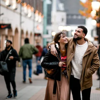 Ein lachendes Paar geht während des Late Night Shopping Arm in Arm durch eine stimmungsvoll beleuchtete Einkaufsstraße. Im Hintergrund sind weitere Besucher zu sehen.