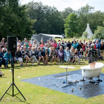 Publiek geniet van een openluchtvoorstelling tijdens Limburg Festival 2025, met een optreden in een badkuip op het gras.
