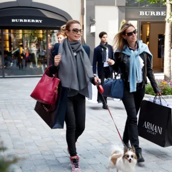 Two women with luxury shopping bags and a small dog stroll past the Burberry and Armani shops during Luxury Days at Designer Outlet Roermond.