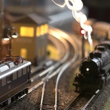 Modeltreinen op een modelspoorbaan tijdens een modeltreinenbeurs, met rook, verlichting en miniatuurhuisjes.