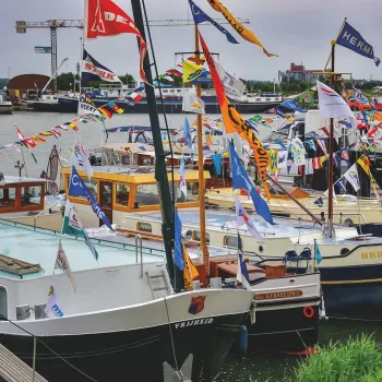 Versierde schepen aangemeerd in de haven van Maasbracht tijdens de Maasbrachter Havendagen, met kleurrijke vlaggen en bezoekers langs het water.